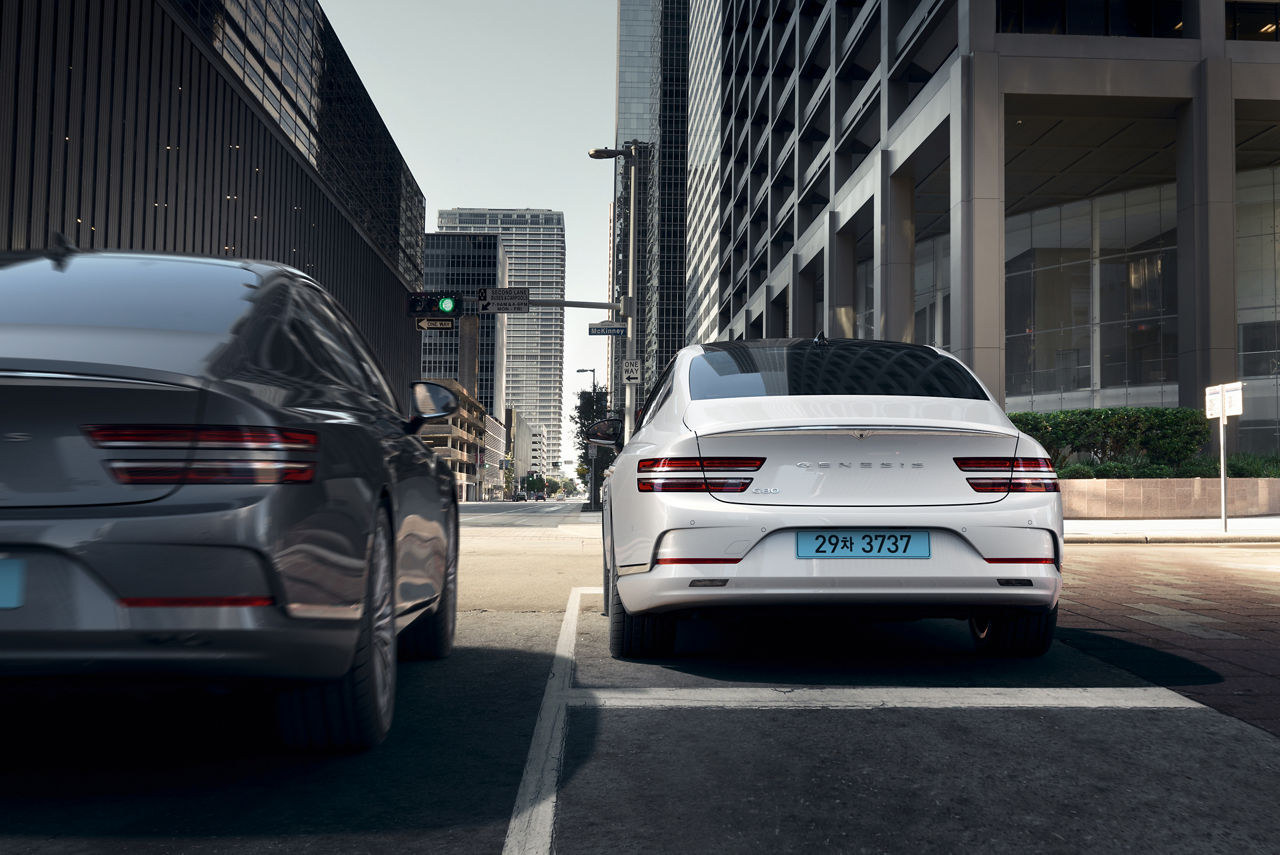 Genesis G80 blanche de dos stationnée dans une rue de la ville, à côté d'une voiture noire