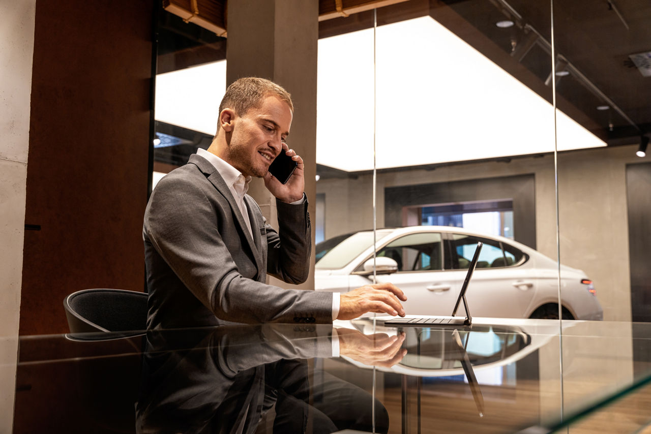 Reflection of a white Genesis in the studio with man sitting at a table with telephone and computer