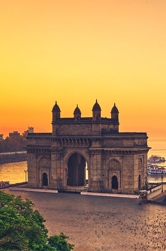 The gateway of India at sunrise with beautiful reflections in the sea. Boats in the water in a hot day.