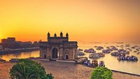 The gateway of India at sunrise with beautiful reflections in the sea. Boats in the water in a hot day.