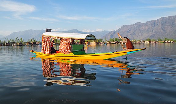 Beautiful view of Shikara boat ride on dal lake with houseboats and mountain background at Srinagar, Kashmir, India.