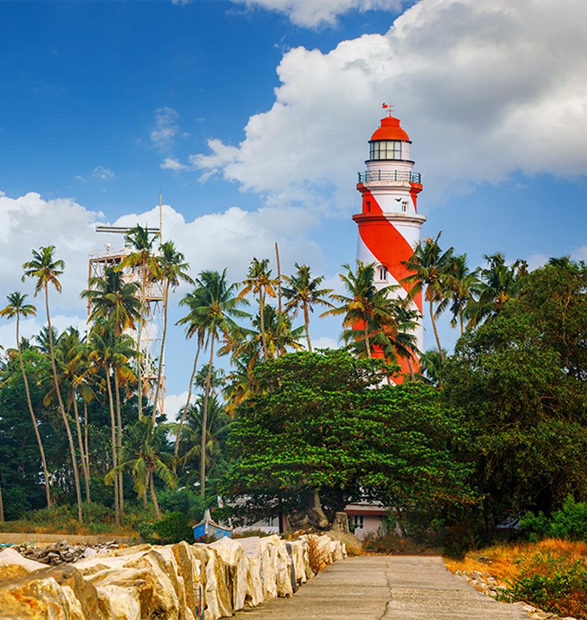 Thangassery red and white stripe Lighthouse on the cliff surrounded by palm trees and big sea waves on the Kollam beach. Kerala, India