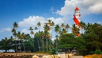 Thangassery red and white stripe Lighthouse on the cliff surrounded by palm trees and big sea waves on the Kollam beach. Kerala, India