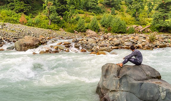 A person sitting on a rock in front of a river in Lidder Valley, at Pahalgam in Kashmir