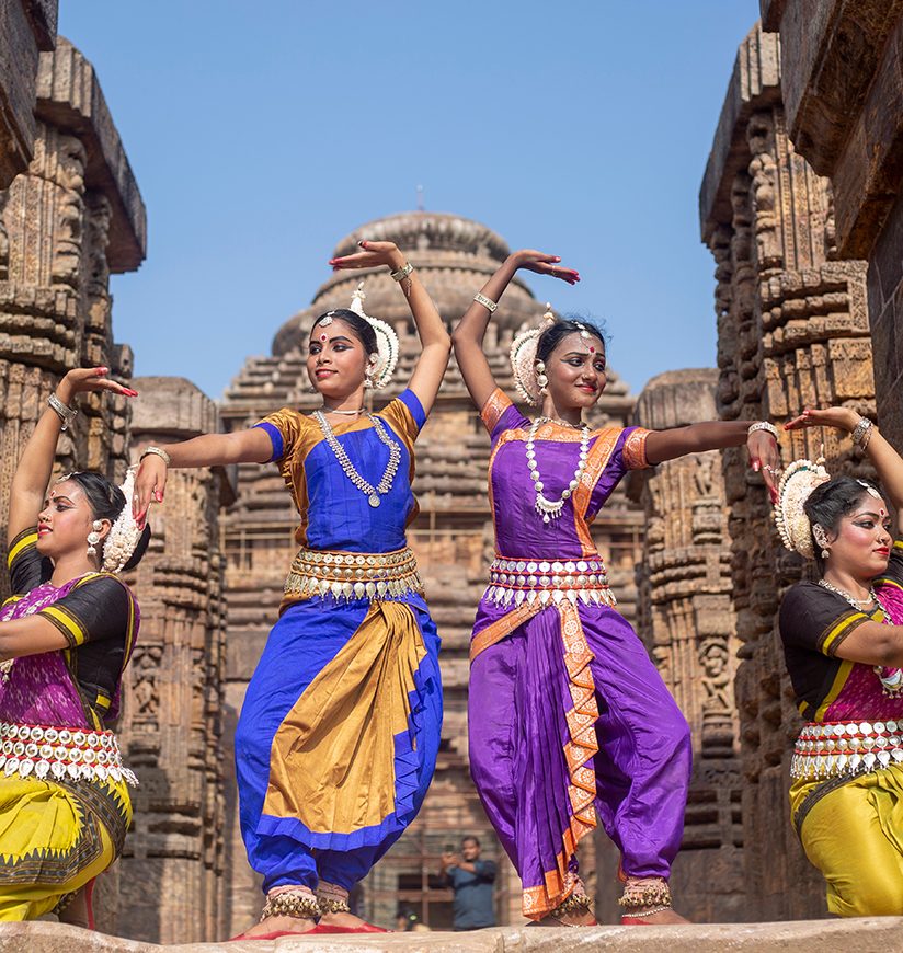 A group of classical odissi dancers wears traditional costume and posing Odissi dance mudra at Konark temple, Odisha, India.