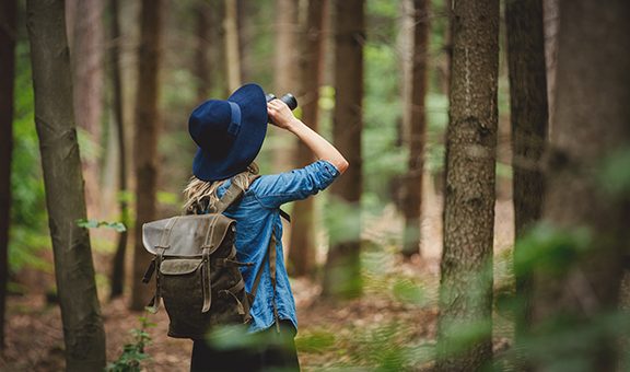 Young woman with binocular and backpack in a forest 