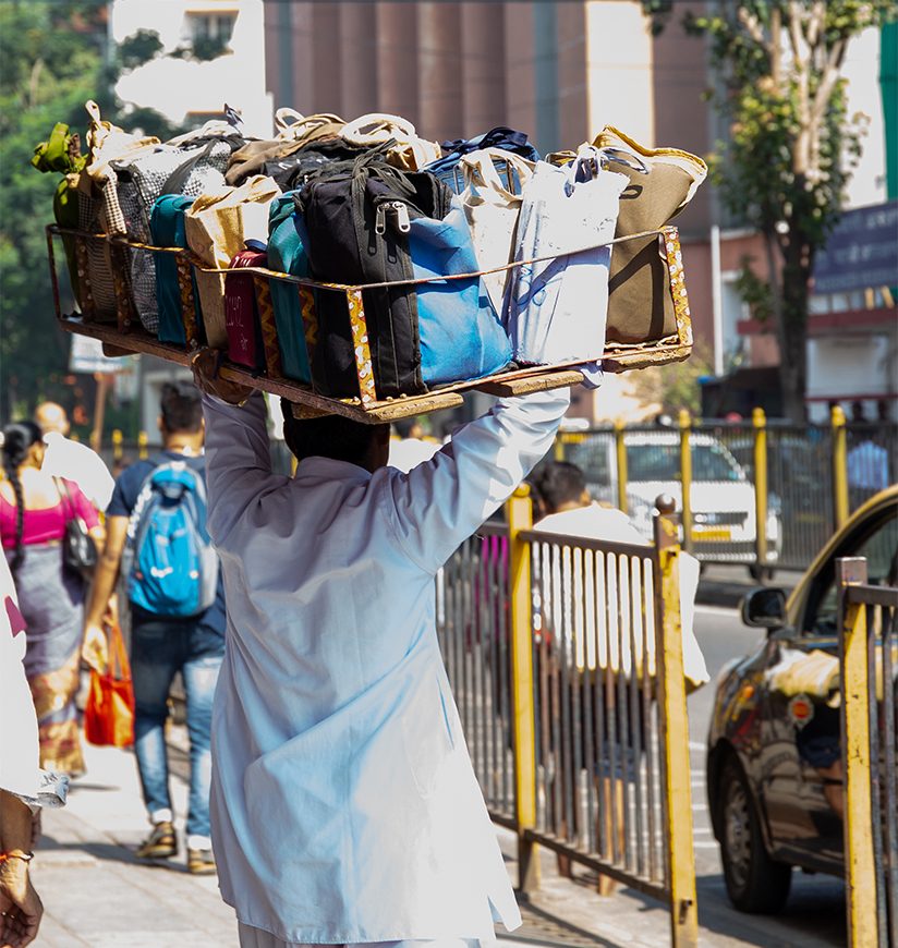 "Dabbawala" lunchbox delivery service in Mumbai, Churchgate Station. Delivery man dressed in white holding lunchboxes on his head.