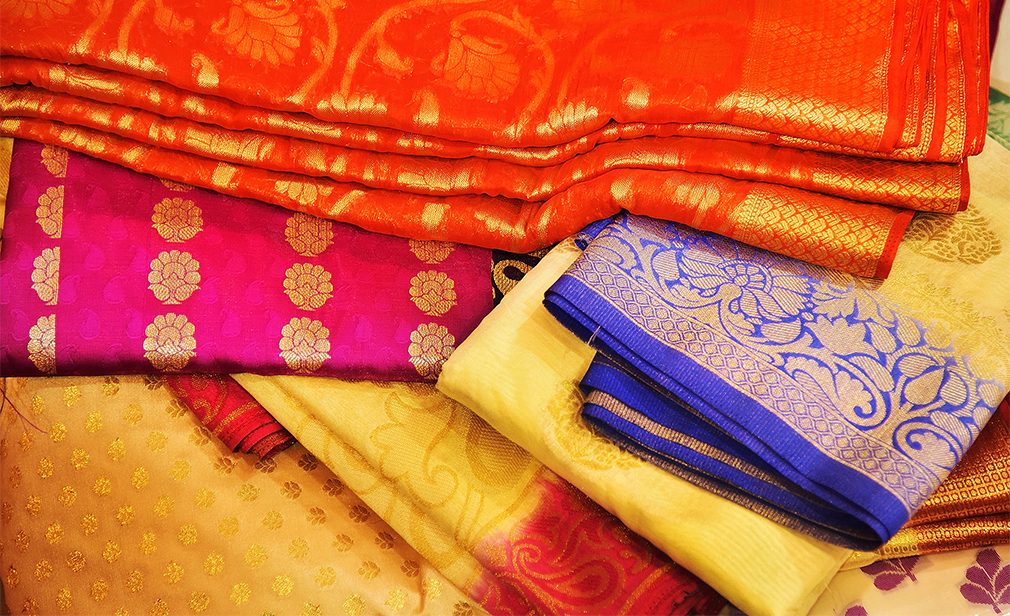 Seamless image of Banares silk saris displayed in front of customers in a textile shop. These exquisite, expensive sarees are famous for their gold and silver zari, brocade. Incredible India.