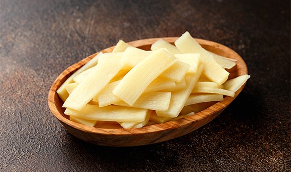 Sliced canned bamboo shoots in wooden bowl.