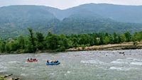 It can be seen in the picture that tourists are enjoying river rafting in the Beas River. The beautiful green mountains of Manali are visible in the background. 