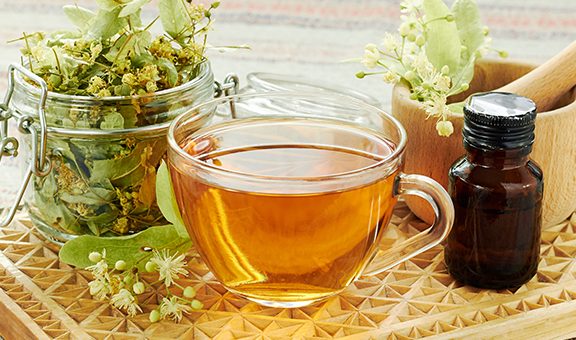 Linden herbal  tea with lime tree bloom and glass can with dried herb nearby on rustic wooden cutting board, backlit, closeup, copy space, alternative medicine and naturopathy concept