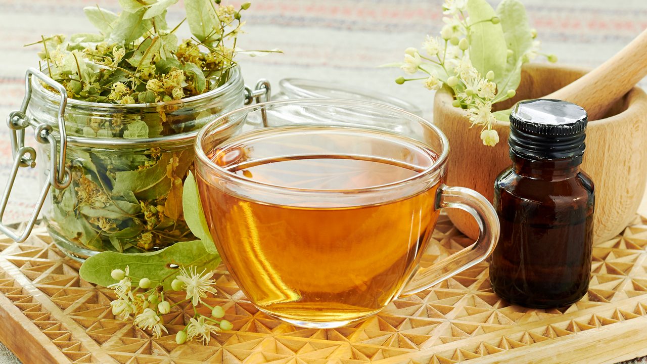 Linden herbal  tea with lime tree bloom and glass can with dried herb nearby on rustic wooden cutting board, backlit, closeup, copy space, alternative medicine and naturopathy concept