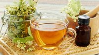 Linden herbal  tea with lime tree bloom and glass can with dried herb nearby on rustic wooden cutting board, backlit, closeup, copy space, alternative medicine and naturopathy concept