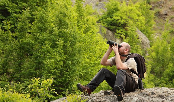 A young man watching birds trought binoculars in the mountain early morning