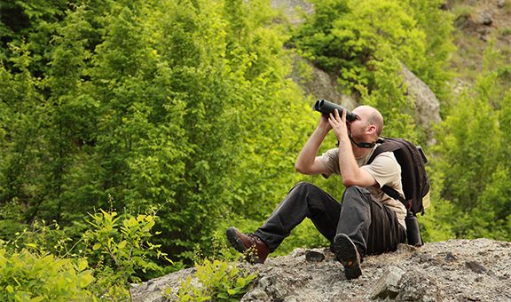 A young man watching birds trought binoculars in the mountain early morning