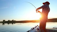 Young man fishing on a lake from the boat at sunset