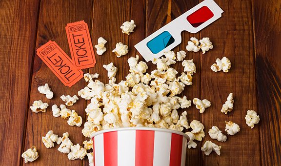 Loose popcorn in striped box, two tickets to the cinema and 3D glasses on a wooden background