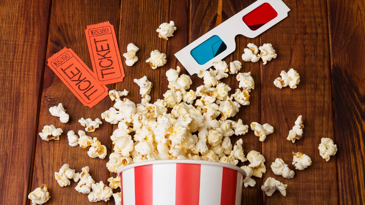 Loose popcorn in striped box, two tickets to the cinema and 3D glasses on a wooden background