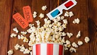 Loose popcorn in striped box, two tickets to the cinema and 3D glasses on a wooden background