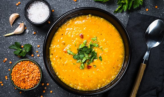 Red lentil soup in black plate on dark stone background. Top view.