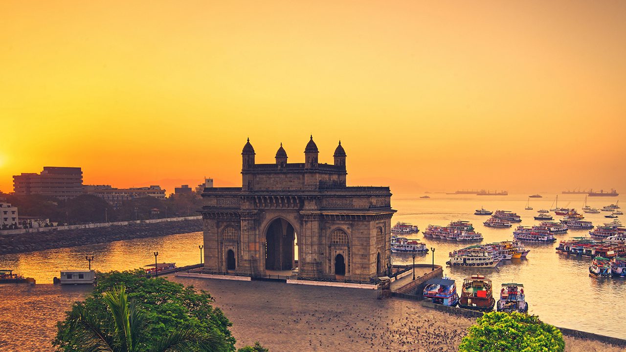 The gateway of India at sunrise with beautiful reflections in the sea. Boats in the water in a hot day.