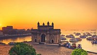 The gateway of India at sunrise with beautiful reflections in the sea. Boats in the water in a hot day.