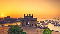 The gateway of India at sunrise with beautiful reflections in the sea. Boats in the water in a hot day.