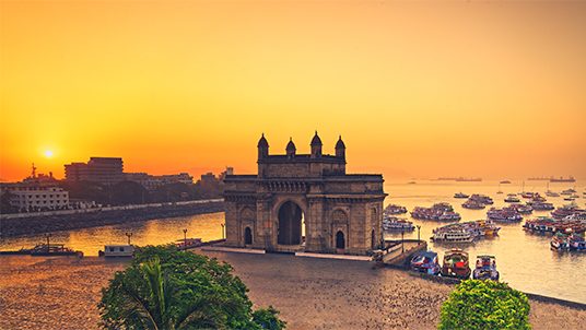 The gateway of India at sunrise with beautiful reflections in the sea. Boats in the water in a hot day.