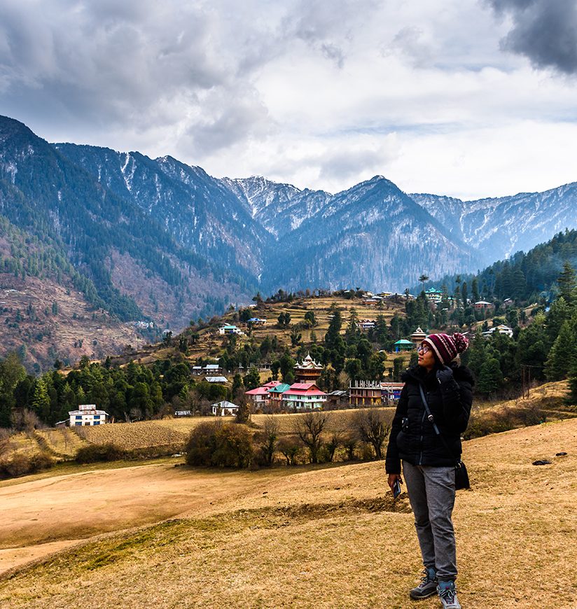 Young woman traveller looking towards the Himalayas mountains in Sainj Valley, Great Himalayan National Park, Himachal