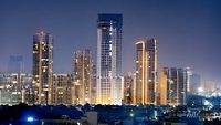 High rise multi story skyscrapers lit up at night with small houses in the foreground at night in gurgaon delhi. Shows the rapid pace of development of the real estate sector with property, offices