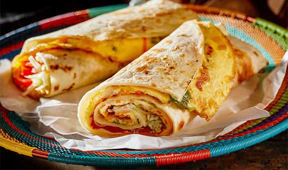 Two delicious indigenous Ugandan Rolex Rolls made with egg omelette and diced fresh vegetables rolled in a chapati or roti on a colorful woven basket