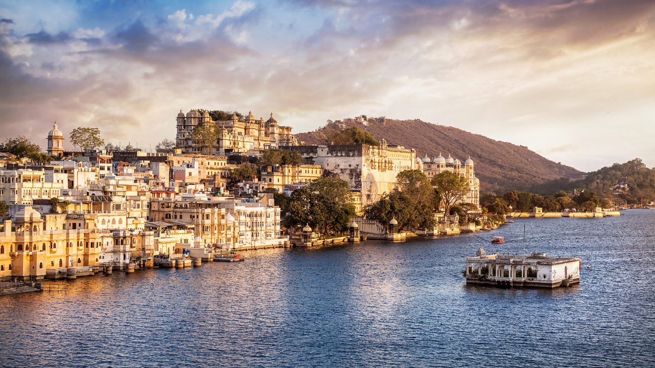 Lake Pichola with City Palace view at cloudy sunset sky in Udaipur, Rajasthan, India