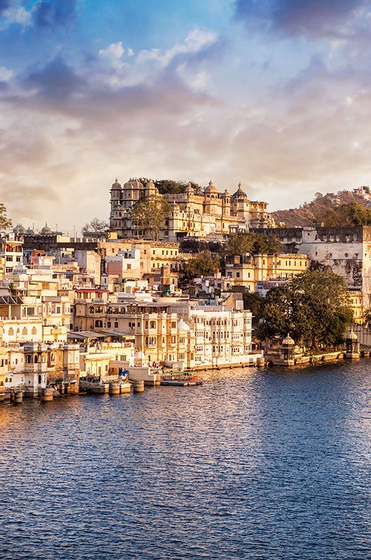 Lake Pichola with City Palace view at cloudy sunset sky in Udaipur, Rajasthan, India