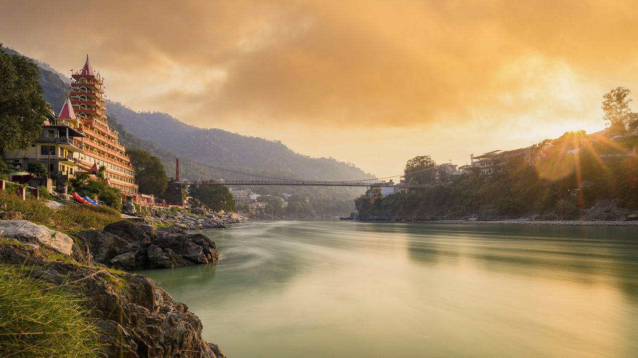 Stunning view of the Ganga river embankment with the Lakshman Jhula bridge and Tera Manzil Temple (Trimbakeshwar) during a beautiful sunset. Rishikesh, Uttarakhand, India.