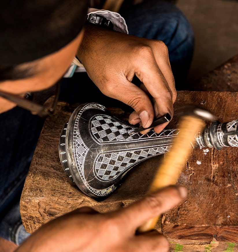 Bidar, Karnataka, India/ December 8, 2018: A Bidri craftsman engraves a traditional design on a vase, its grooves which will then be filled with fine silver wire.