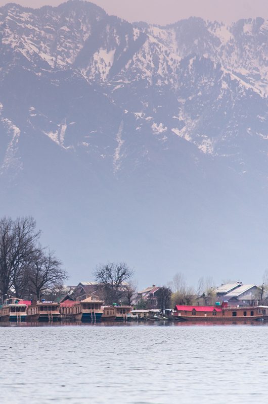 Morning scene of Nigeen lake with the native boat man and the small town behind the mountain range. 