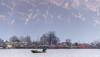 Morning scene of Nigeen lake with the native boat man and the small town behind the mountain range. 