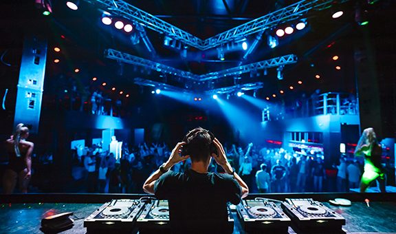 DJ with headphones at night club party under the blue light and people crowd in background