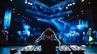 DJ with headphones at night club party under the blue light and people crowd in background