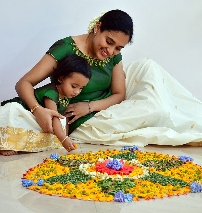 A young lady helping her daughter in making Pookalam for Onam celebrations.