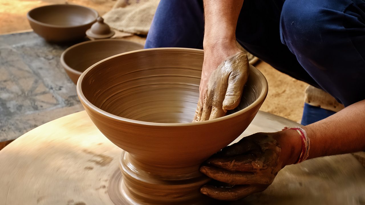 Pottery - skilled wet hands of potter shaping the clay on potter wheel. Pot, vase throwing. Manufacturing traditional handicraft Indian bowl, jar, pot, jug. Shilpagram, Udaipur, Rajasthan, India