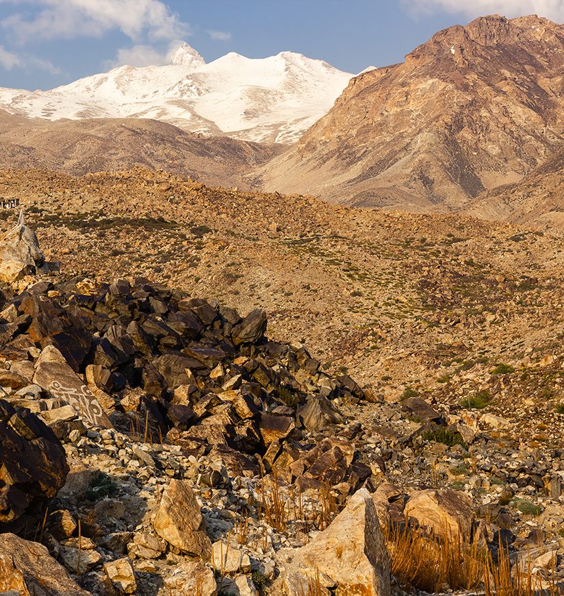 A snow capped Himalayan peak towering over the rocky slopes of the dry, barren mountains in the village of Nako in Kinnaur in Himachal Pradesh, India.