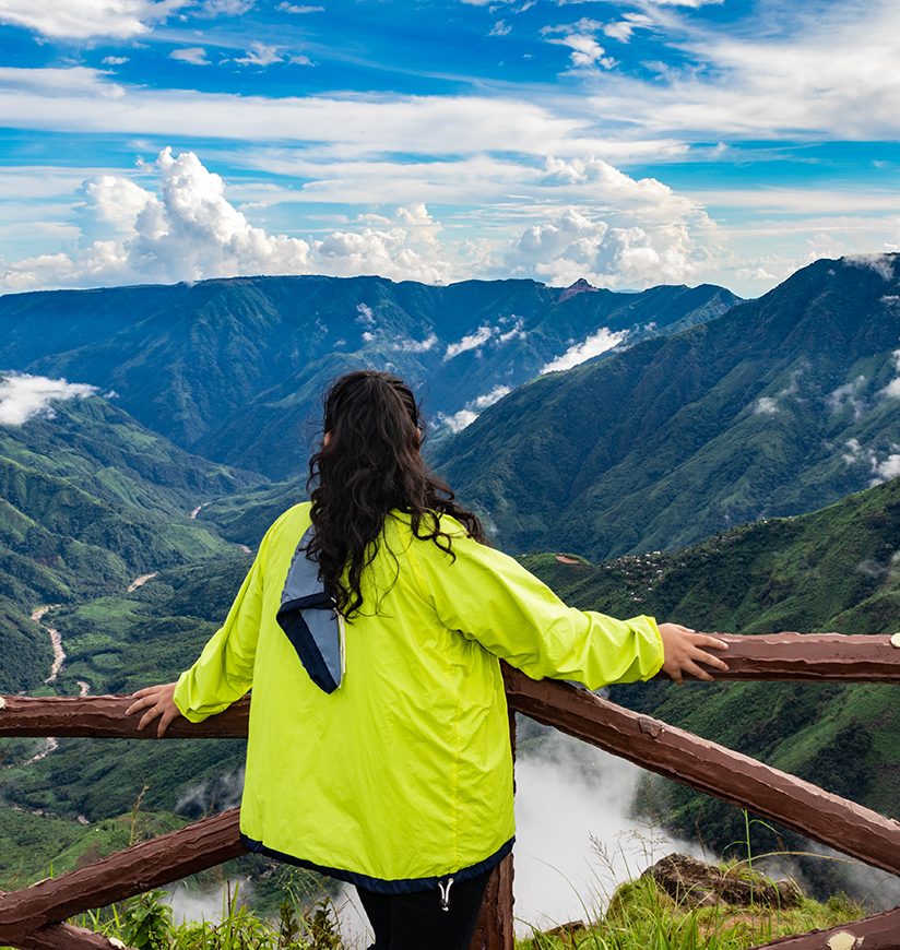 isolated young girl watching mountain valley filled with low cloud and dramatic sky at morning image is taken at latilum peak shillong meghalaya india.