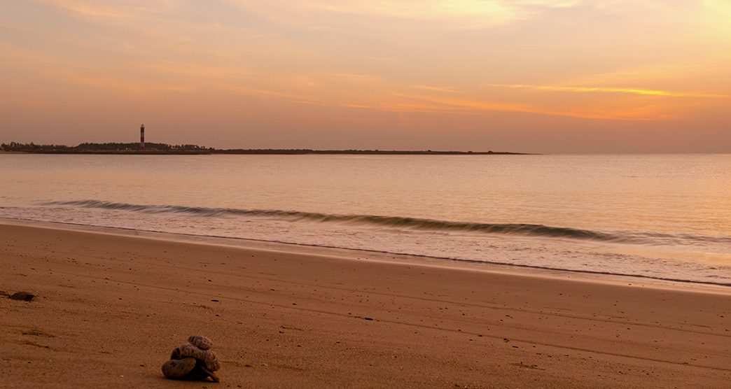 Sunset at Shivrajpur beach dwarka gujarat. Shows the very beauitful beach with its beautiful sand, waves lapping the shore, clouds and the lighthouse in the distance. Light changes from golden to cool