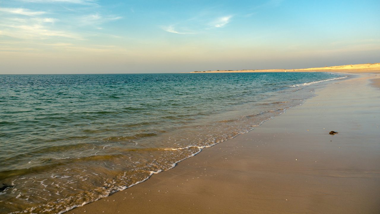 Shivrajpur beach near dwarka gujarat india at dusk with bue arabian sea and the waves of the ocean. The expansive landscape and the clouds on the blue sky over the deserted beach show how untouched