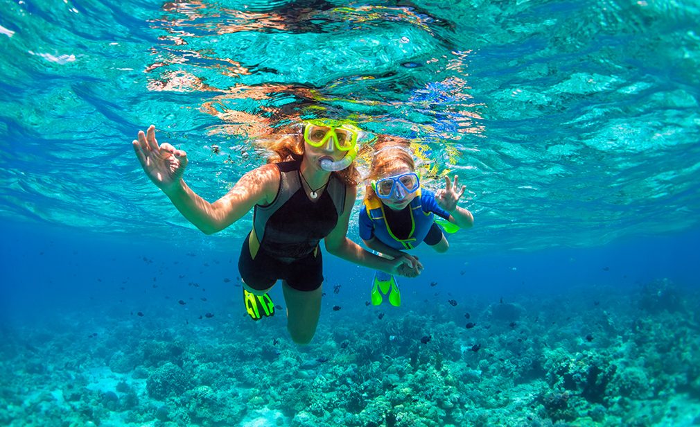 Happy family - mother, kid in snorkeling mask dive underwater with tropical fishes in coral reef sea pool. Show by hands divers sign OK. Travel lifestyle, beach adventure on summer holiday with child.