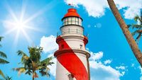 Thangassery red and white stripe Lighthouse on the cliff surrounded by palm trees and big sea waves sun rays on the Kollam beach. Kerala, India