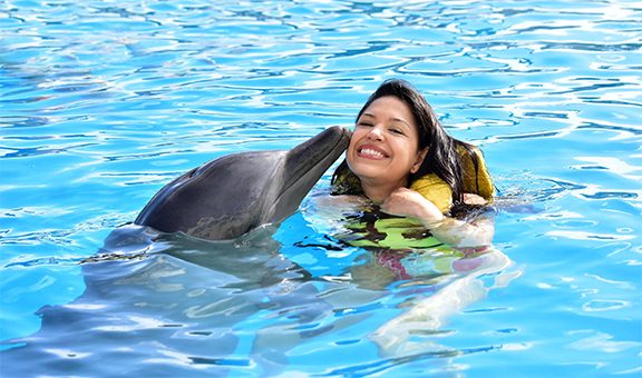 Smiling young woman kissing dolphin in pool.