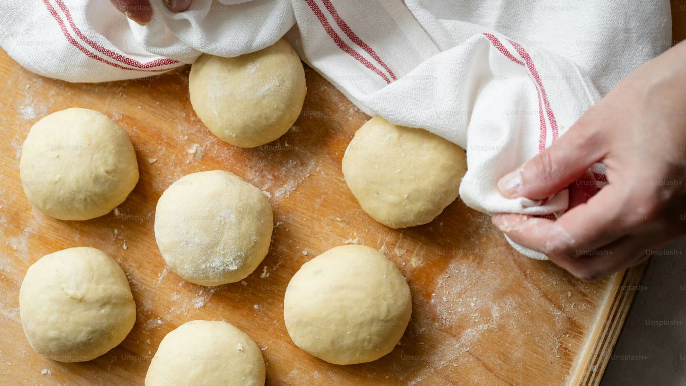 Fresh dough balls resting under kitchen towel