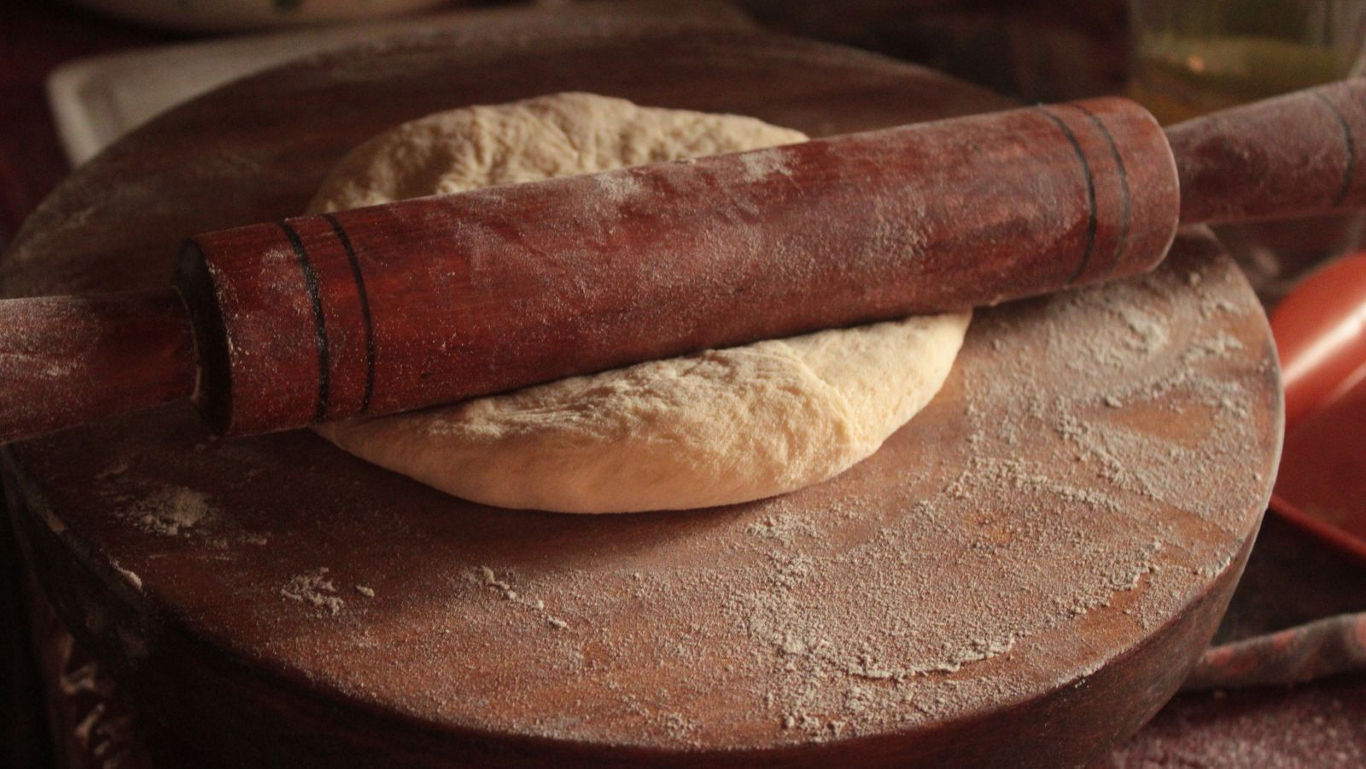 Wooden rolling pin flattening dough on board